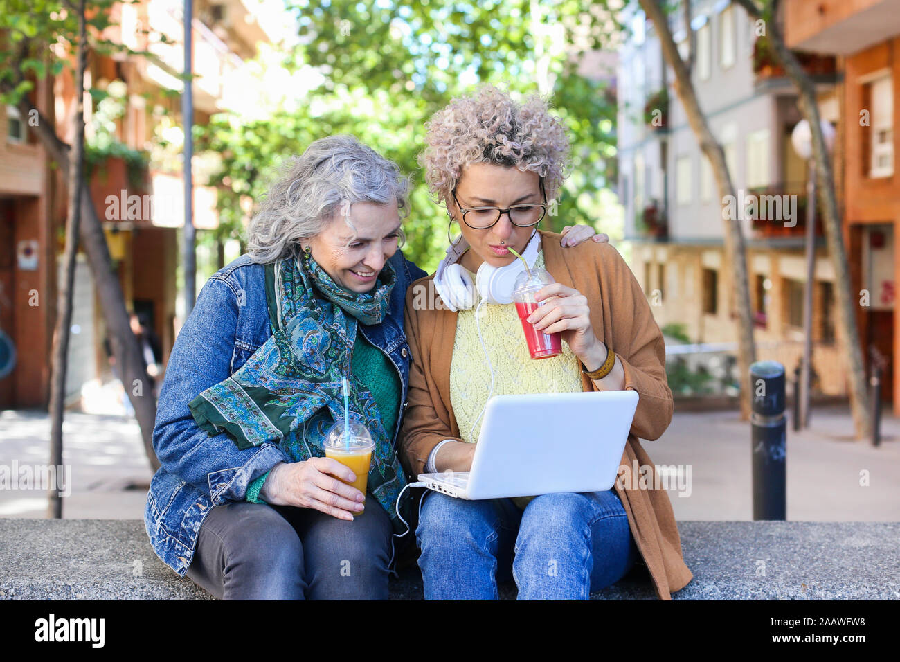 Senior mother with her adult daughter using laptop and drinking juices in the city Stock Photo