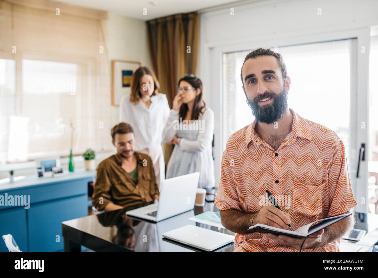 Portrait of smiling man holding notebook with friends in background Stock Photo