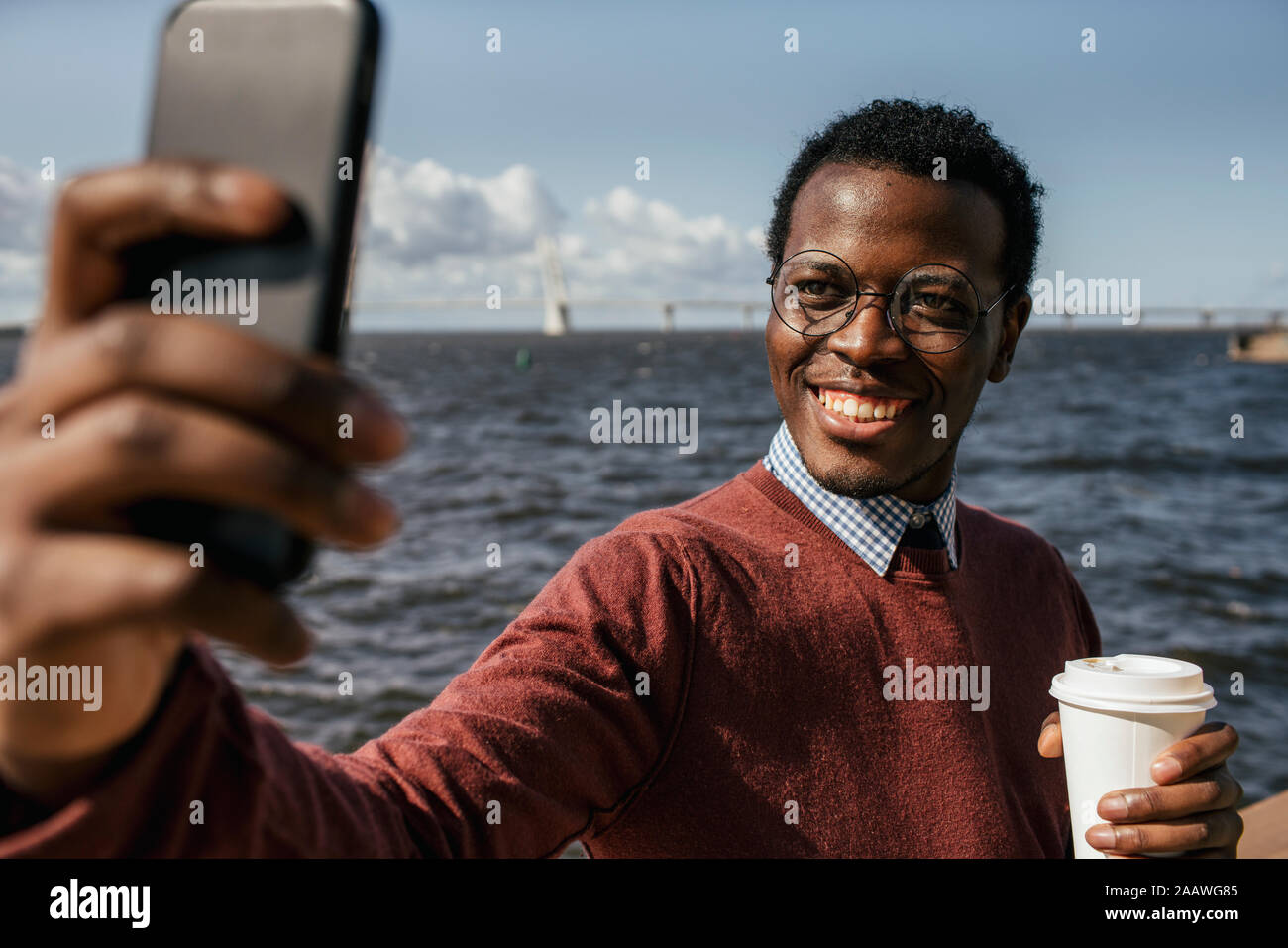 Young man taking smartphone selfie at the sea, holding take out coffee Stock Photo