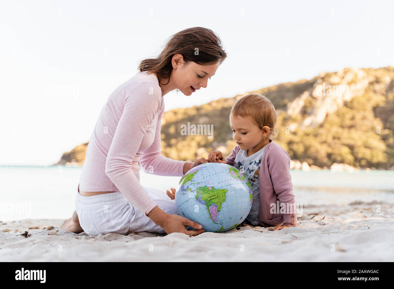 Woman and little daughter sitting on the beach looking together at Earth beach ball Stock Photo