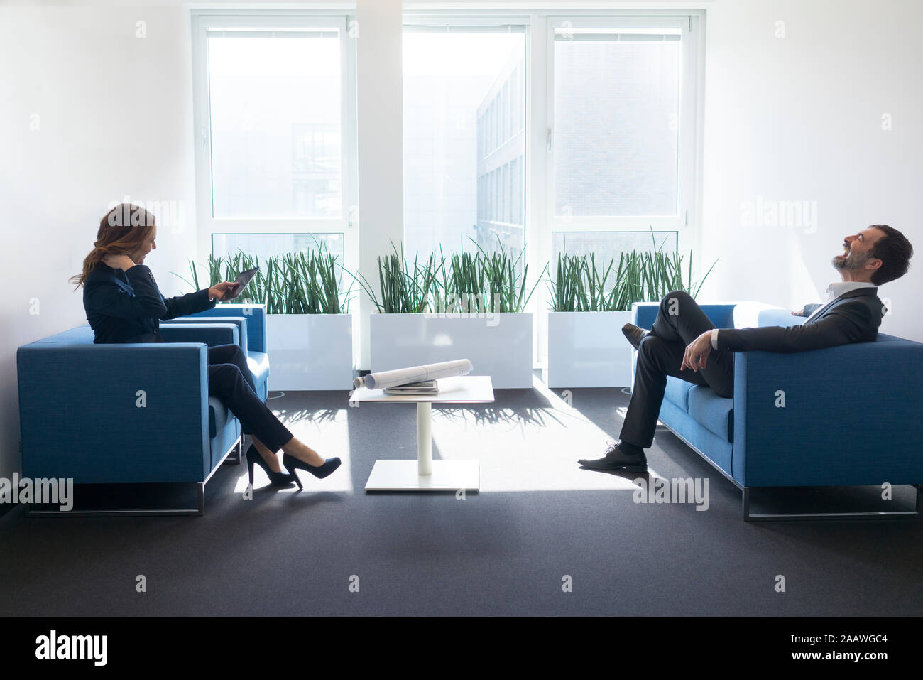 Laughing businesswoman and businessman sitting in office lounge Stock Photo