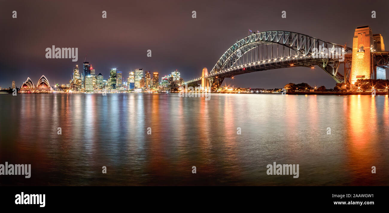 Panoramic shot of illuminated Sydney Harbor Bridge over river against sky at night, Sydney, Australia Stock Photo