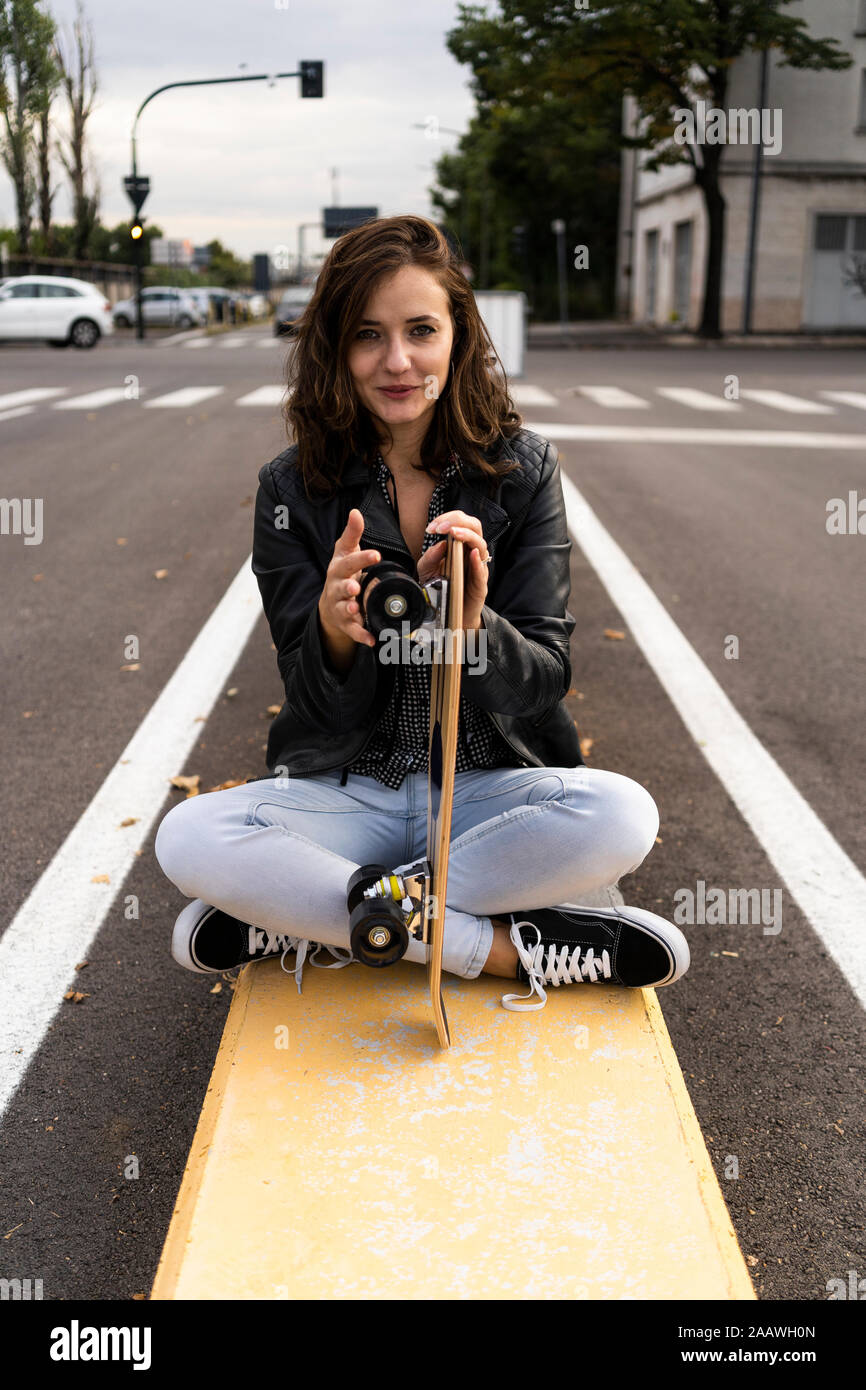 Portrait of smiling young woman with skateboard sitting on bollard Stock Photo
