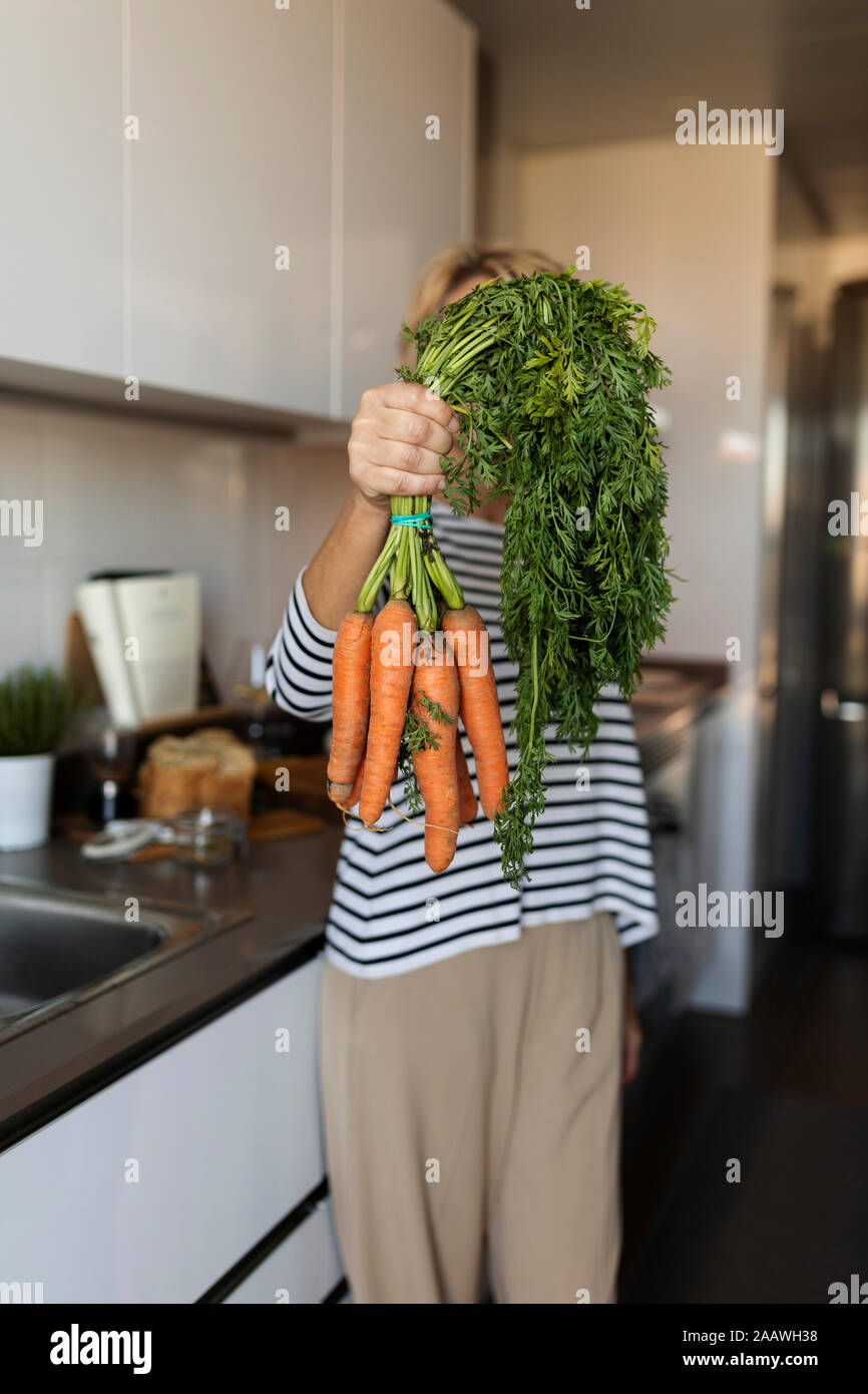 Woman holding a bunch of carrots in kitchen at home Stock Photo