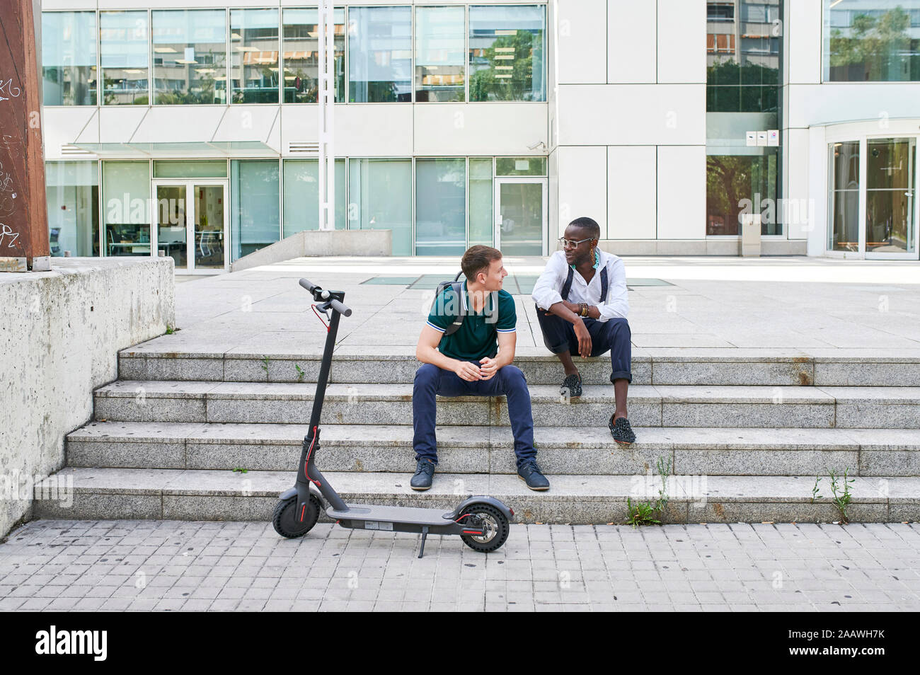 Two casual businessmen talking on stairs in the city next to e-scooter Stock Photo