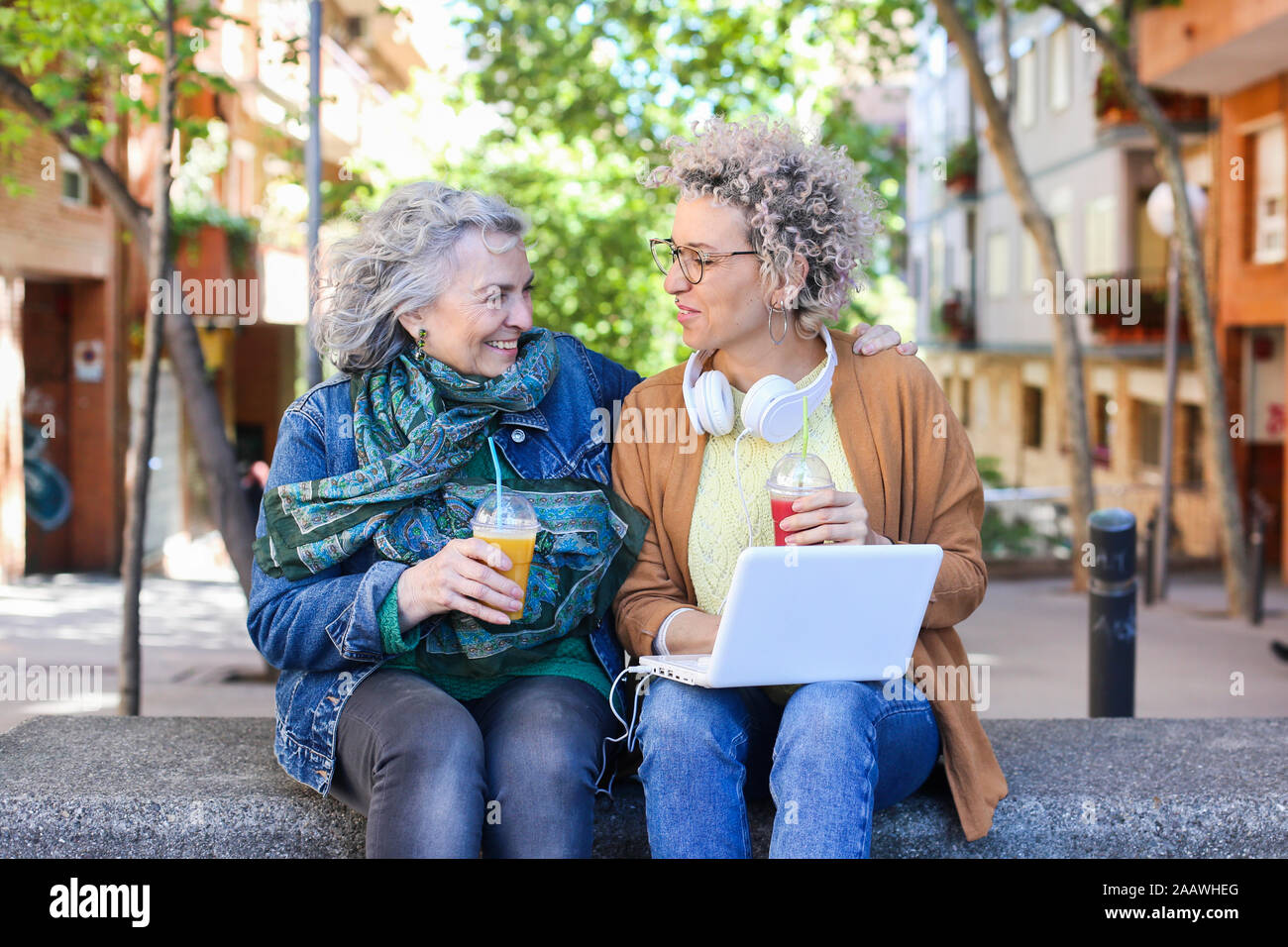Senior mother with her adult daughter using laptop and drinking juices in the city Stock Photo