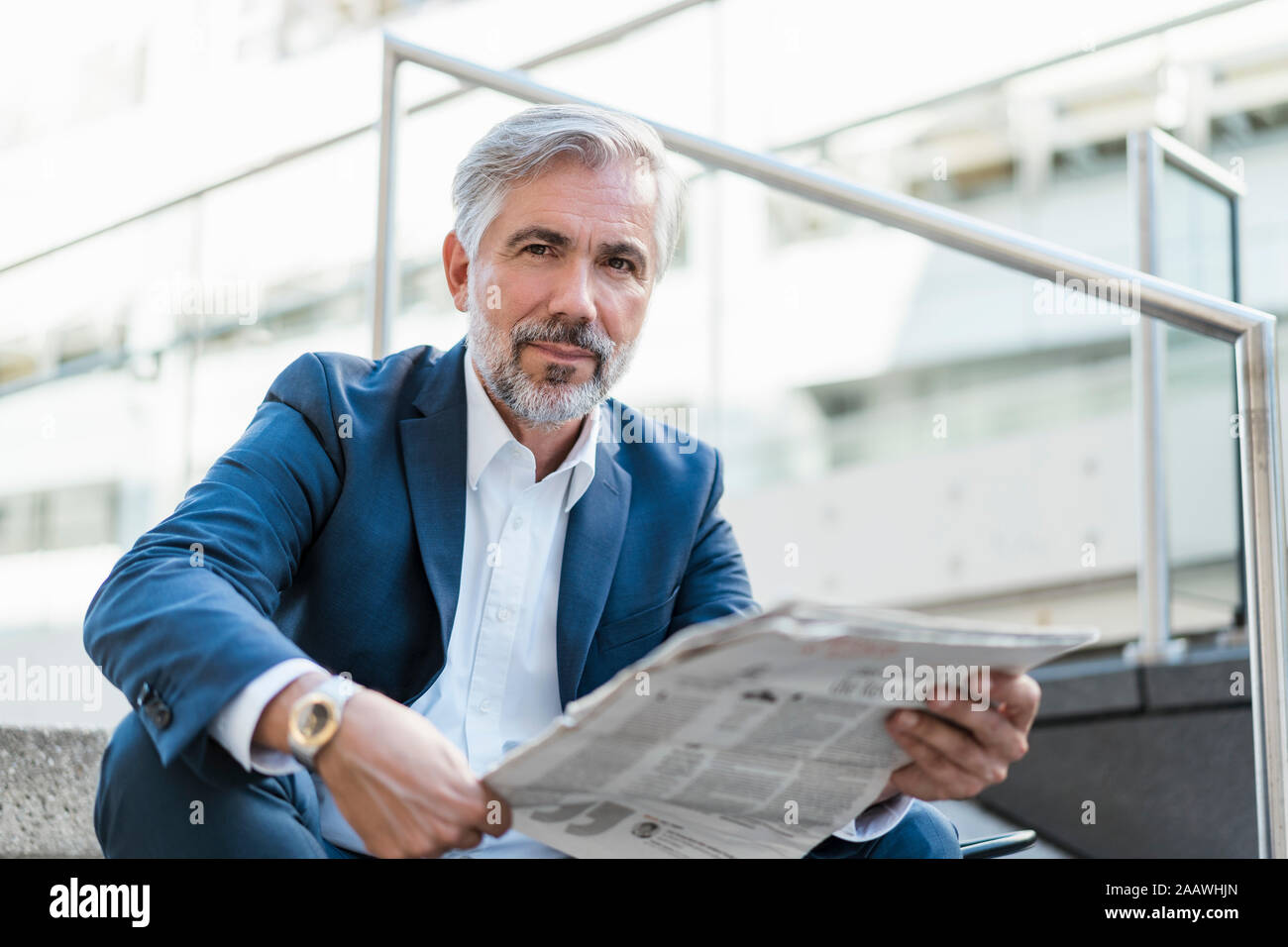 Portrait of mature businessman sitting on stairs in the city with newspaper Stock Photo