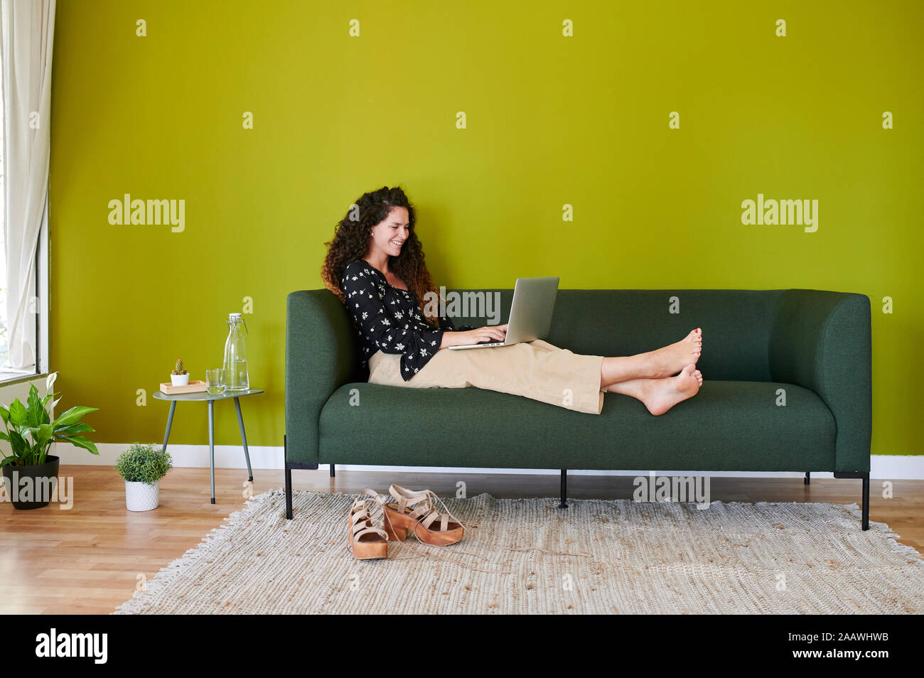 Smiling young businesswoman using laptop on couch in modern office Stock Photo