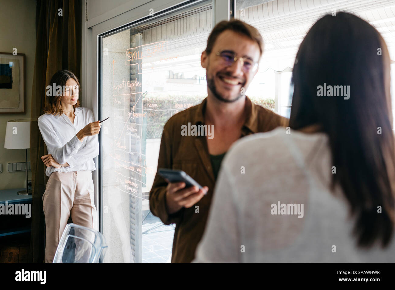 Woman writing on glass pane with coworkers in foreground Stock Photo