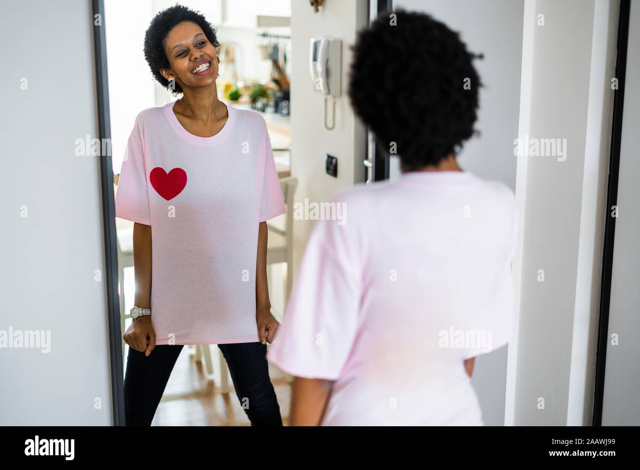 Happy young woman wearing t-shirt with heart shape looking in mirror Stock Photo