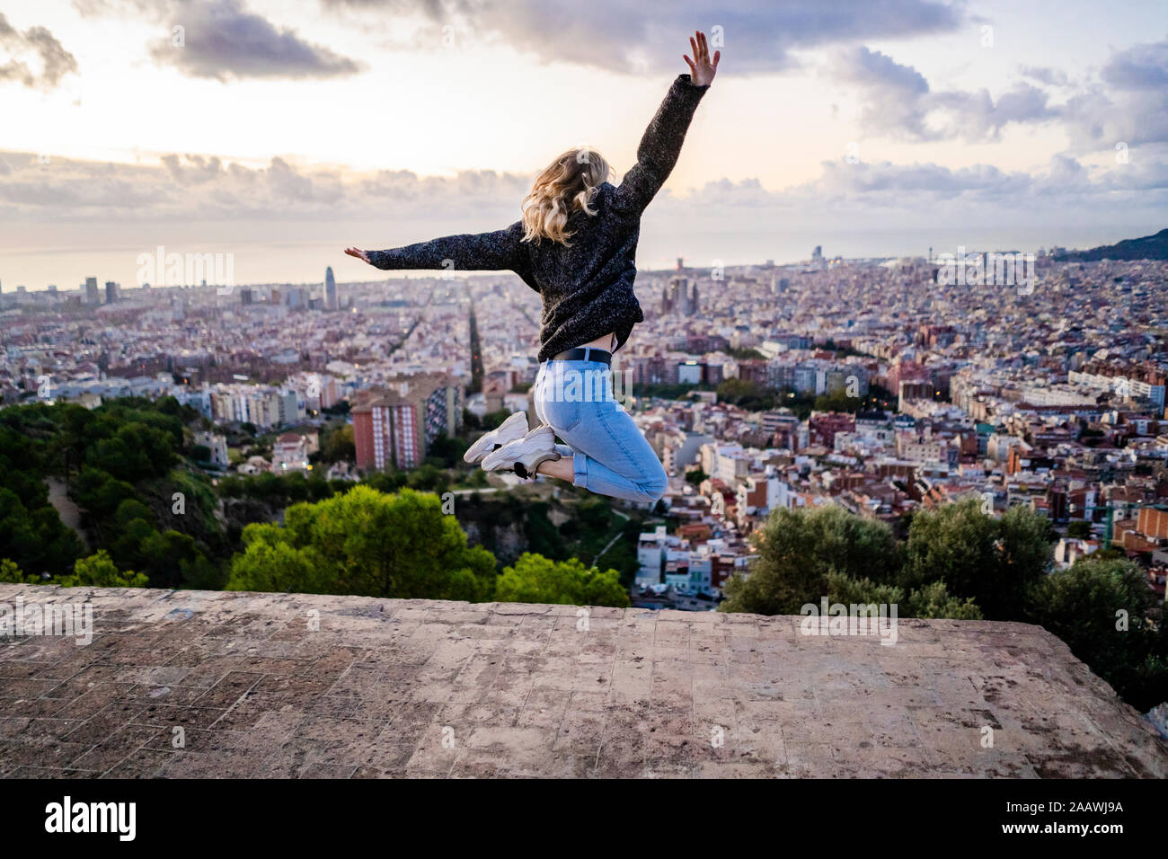Carefree young woman jumping above the city at sunrise, Barcelona, Spain Stock Photo