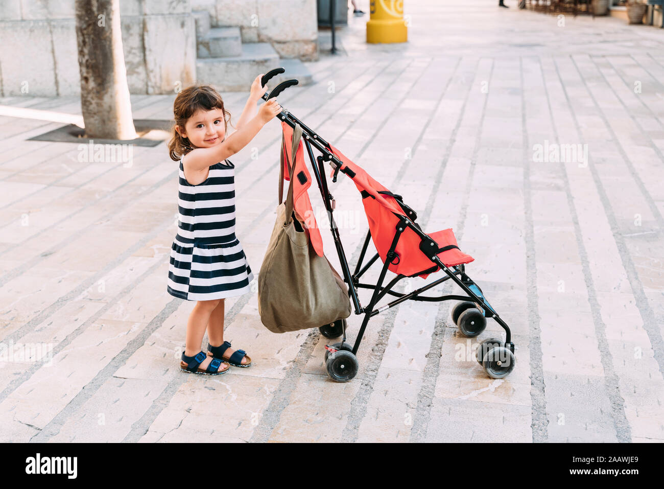 Portrait of smiling little girl pushing her stroller Stock Photo