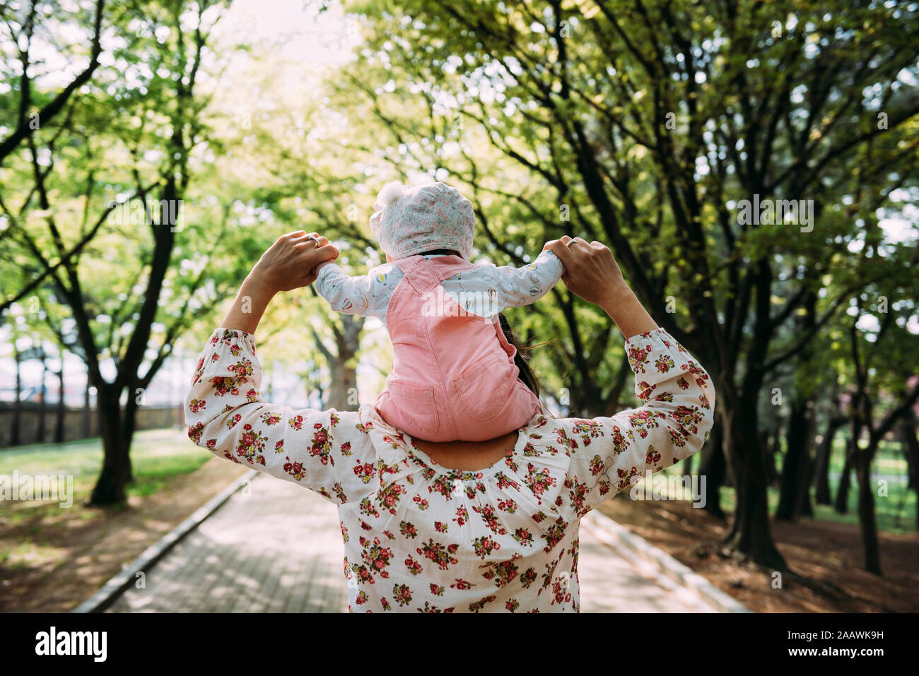 Mother walking in a park with baby girl on her shoulders Stock Photo