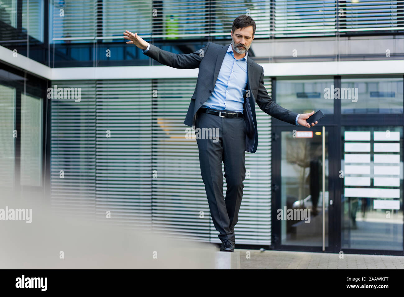 Mature businessman balancing on a wall outside office building Stock Photo