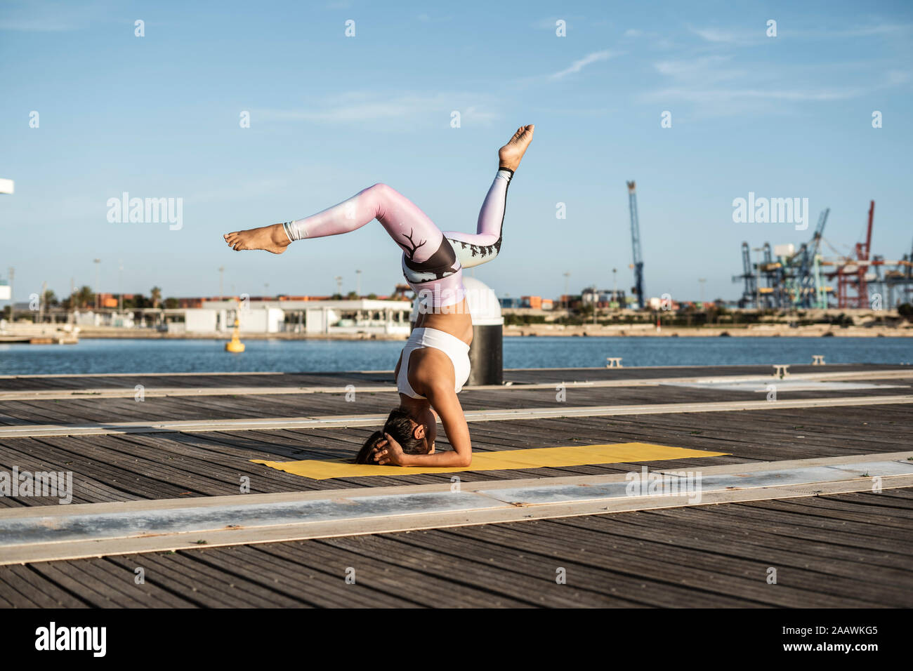 Asian woman practicing yoga on a pier at harbour at sunset, swan pose stock  photo