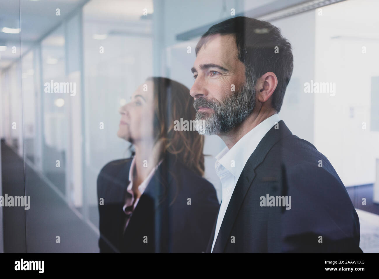 Portrait of businesswoman and businessman in office looking through glass pane Stock Photo