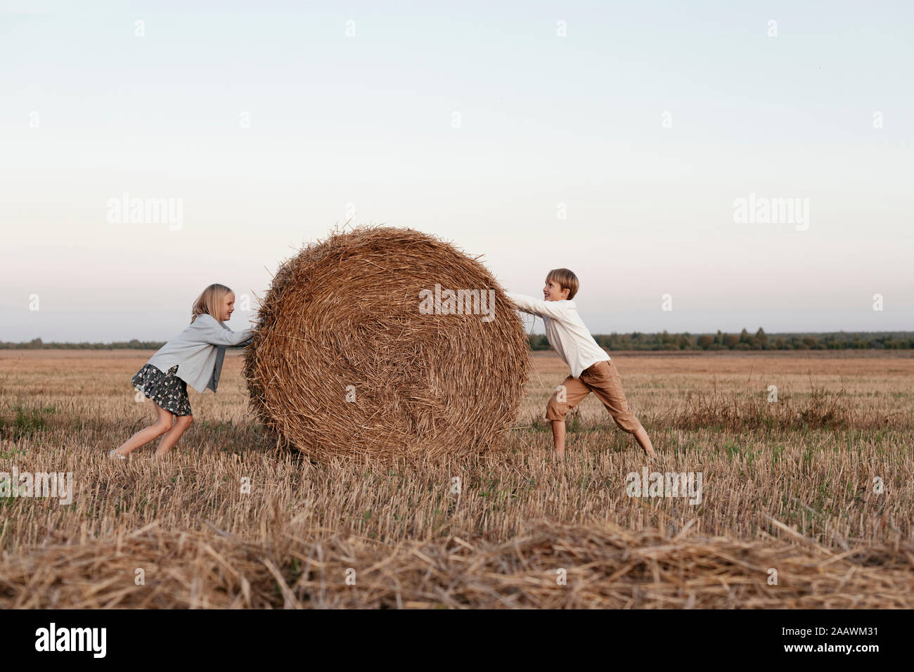 Two kids rolling a haystack on the field Stock Photo
