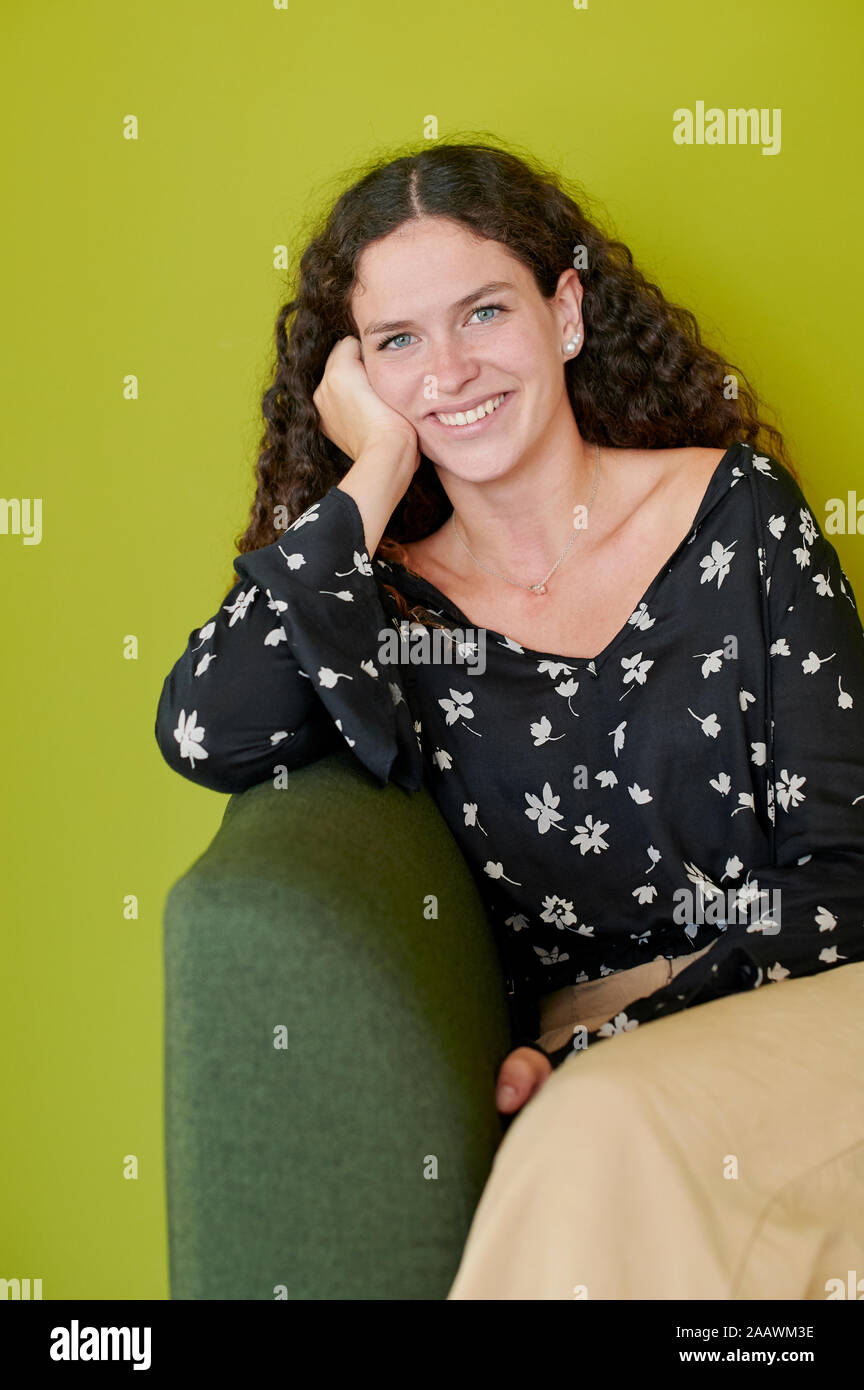 Portrait of smiling young woman sitting on green couch Stock Photo