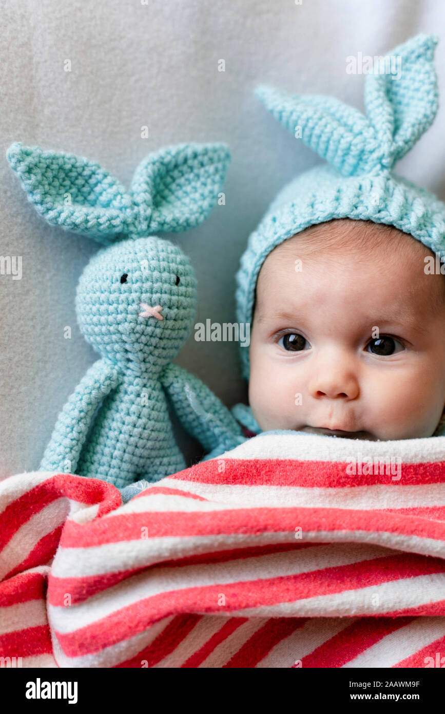 Baby girl with bunny hat and a bunny toy on bed with a blanket Stock Photo