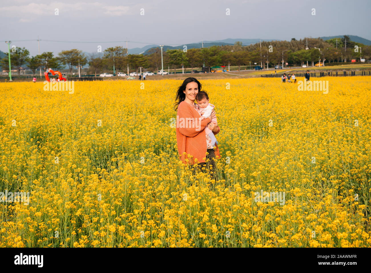 Portrait of happy woman with baby girl on her arms standing in a rape field, Gyeongju, South Korea Stock Photo