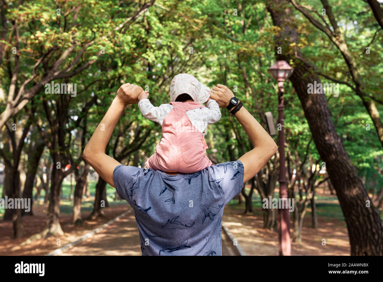 Father walking in a park with baby girl on his shoulders Stock Photo