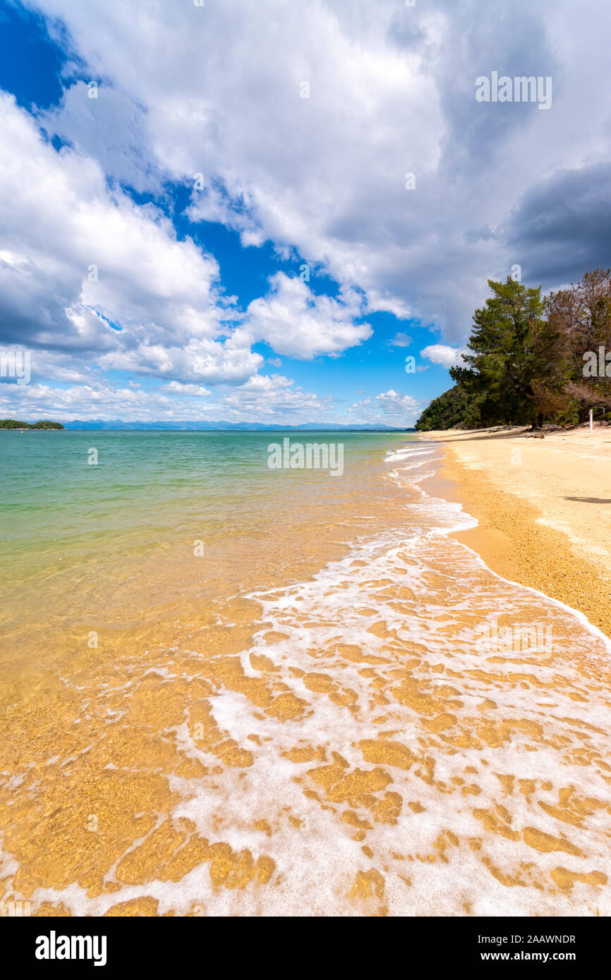 Scenic view of beach against cloudy sky during sunny day at Abel Tasman Coastal Track, South Island, New Zealand Stock Photo