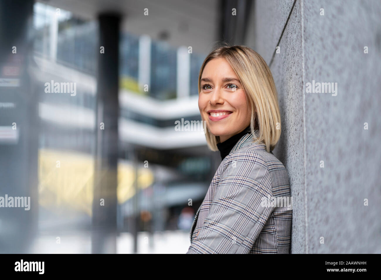 Portrait of smiling young businesswoman leaning against a wall Stock Photo