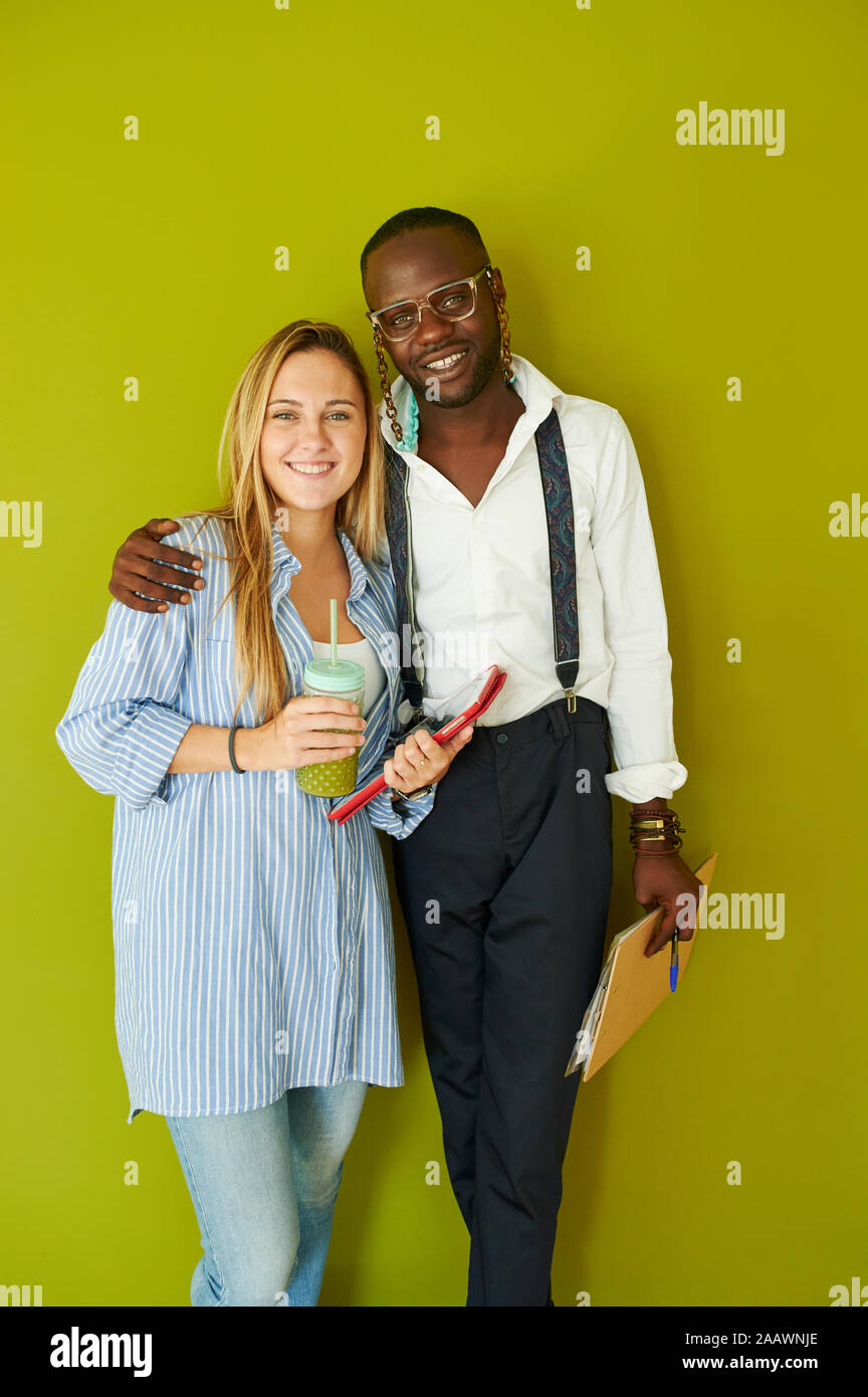 Portrait of smiling casual business couple standing together in front of a green wall Stock Photo