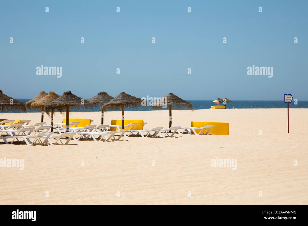 Thatched roof parasols and lounge chairs at sandy beach against clear sky, Albufeira, Algarve, Portugal Stock Photo
