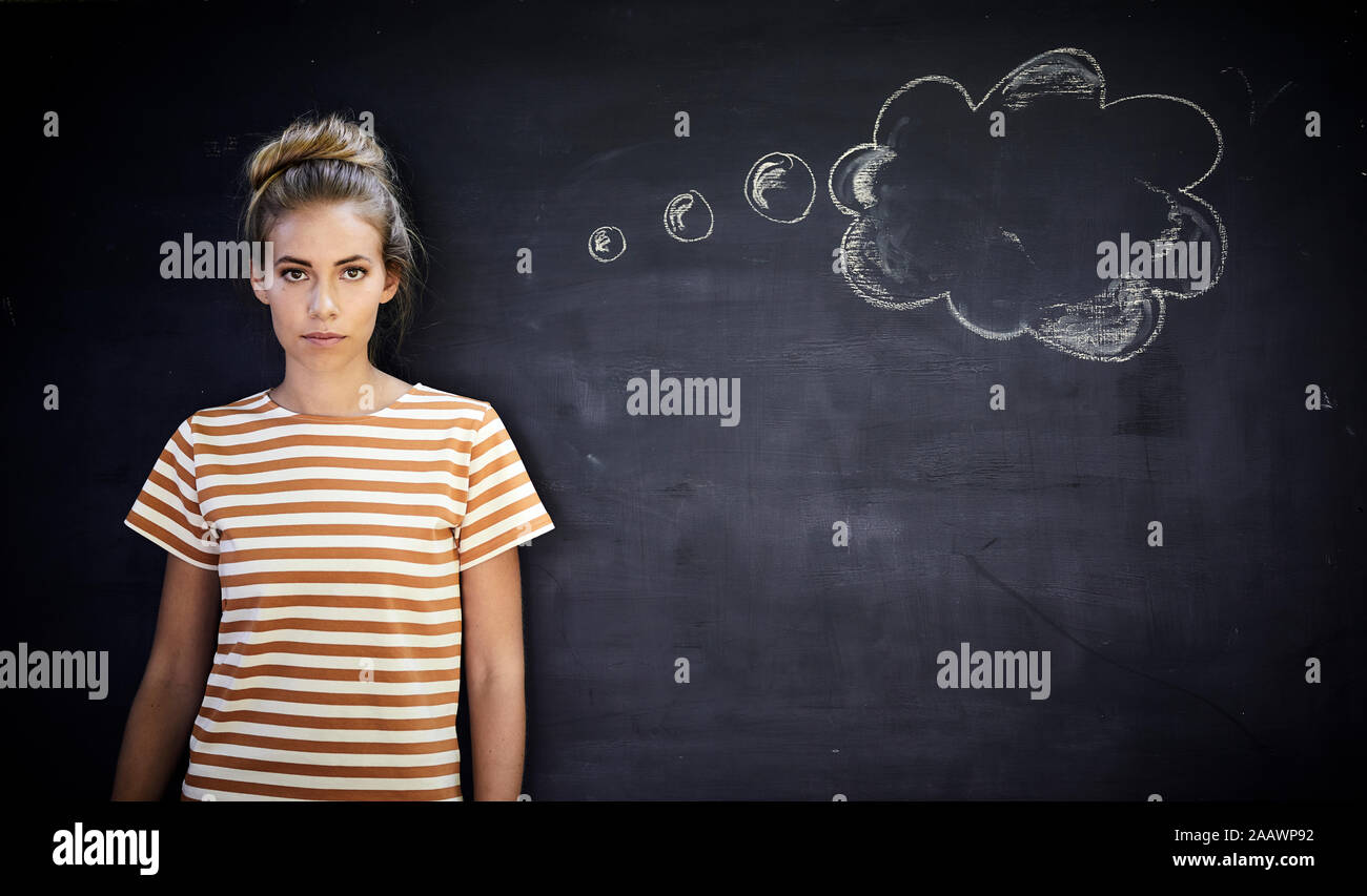 Pensive young woman standing in front of a blackboard next to a thought bubble Stock Photo