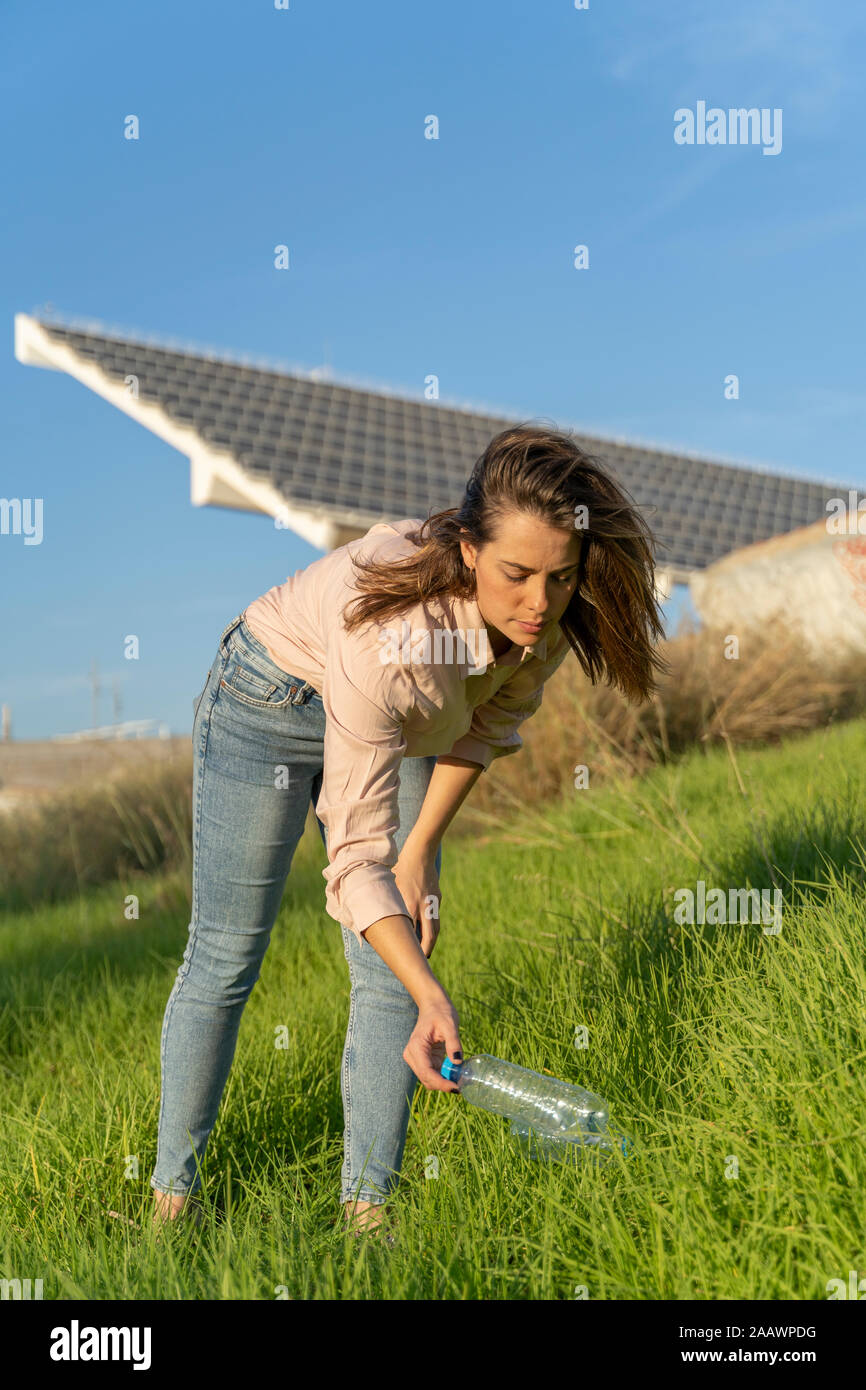 Woman on a meadow picking up empty plastic bottle Stock Photo