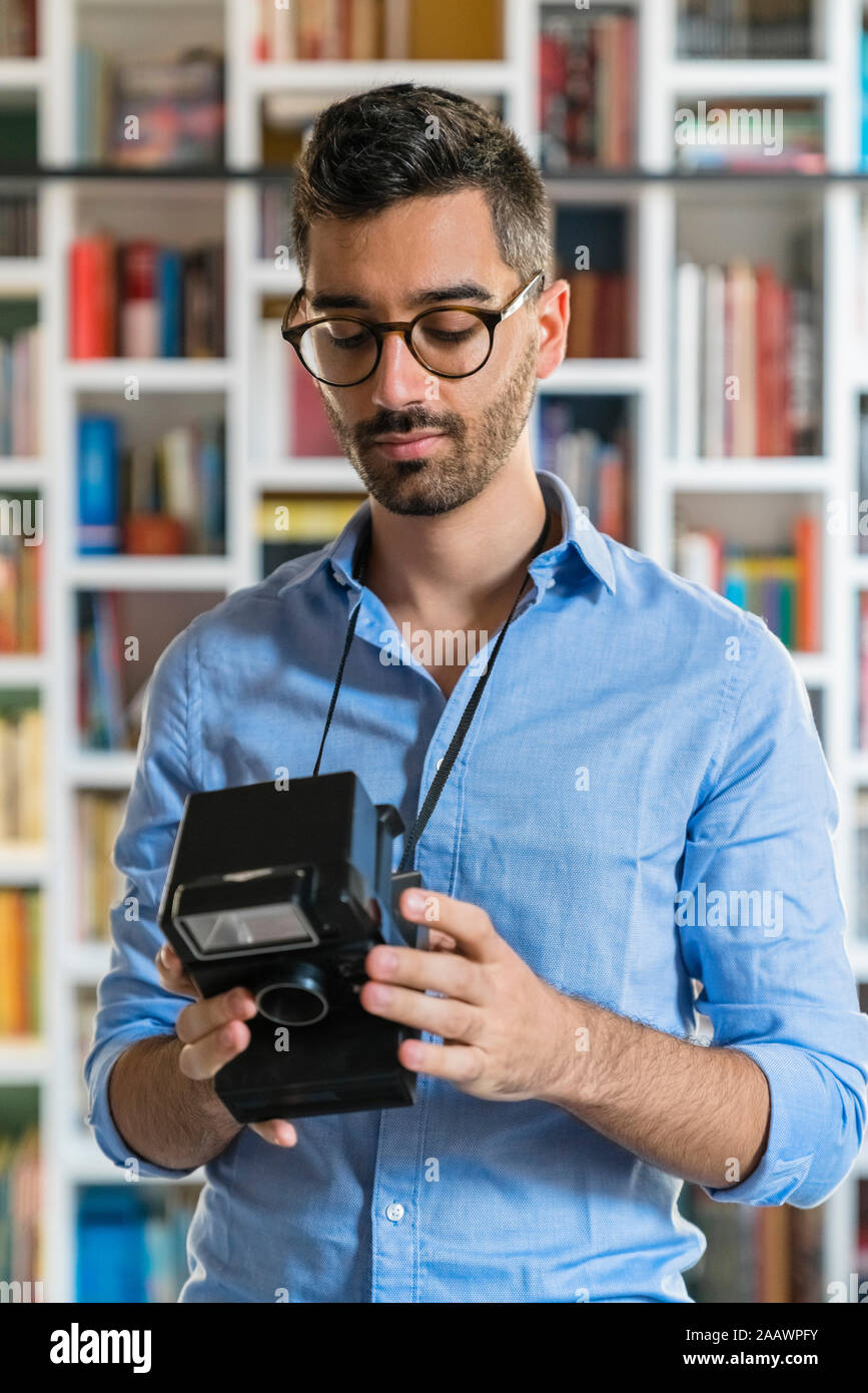 Portrait of young man standing in front of bookshelves looking at instant camera Stock Photo