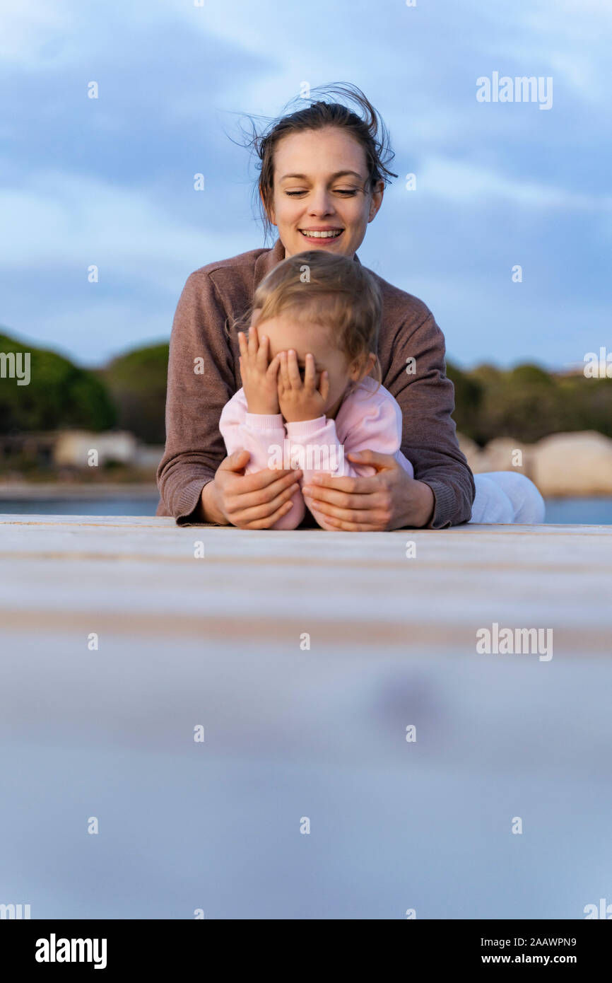 Happy mother with daughter lying on a jetty at sunset Stock Photo