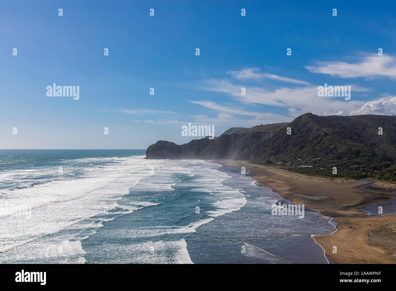 Scenic view of cliff by sea against blue sky at Piha Beach, Auckland, New Zealand Stock Photo