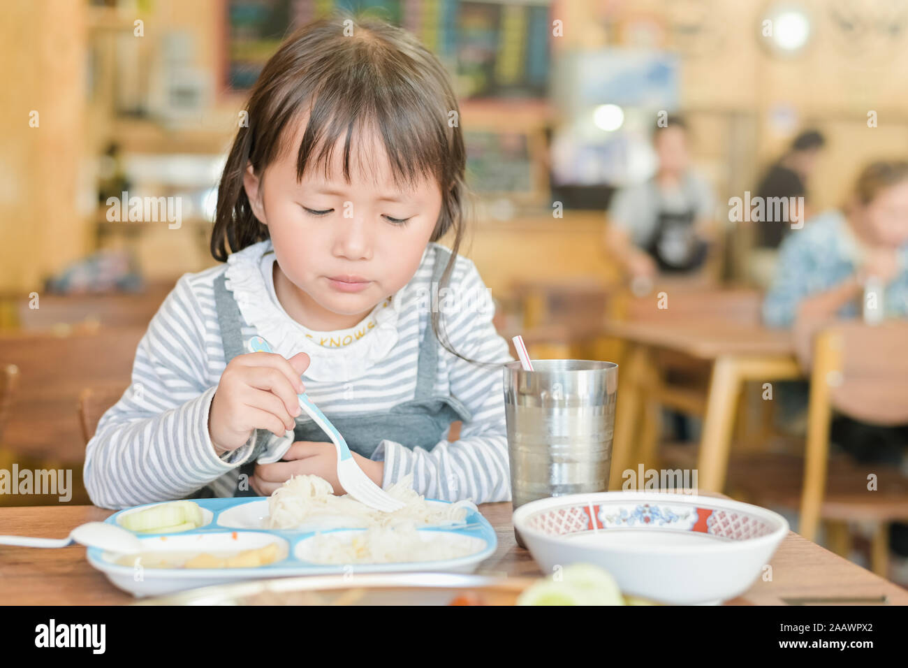 Little asian child girl with unhappy face while having lunch on table in restaurant,picky eater don't want to eat or Not hungry Stock Photo