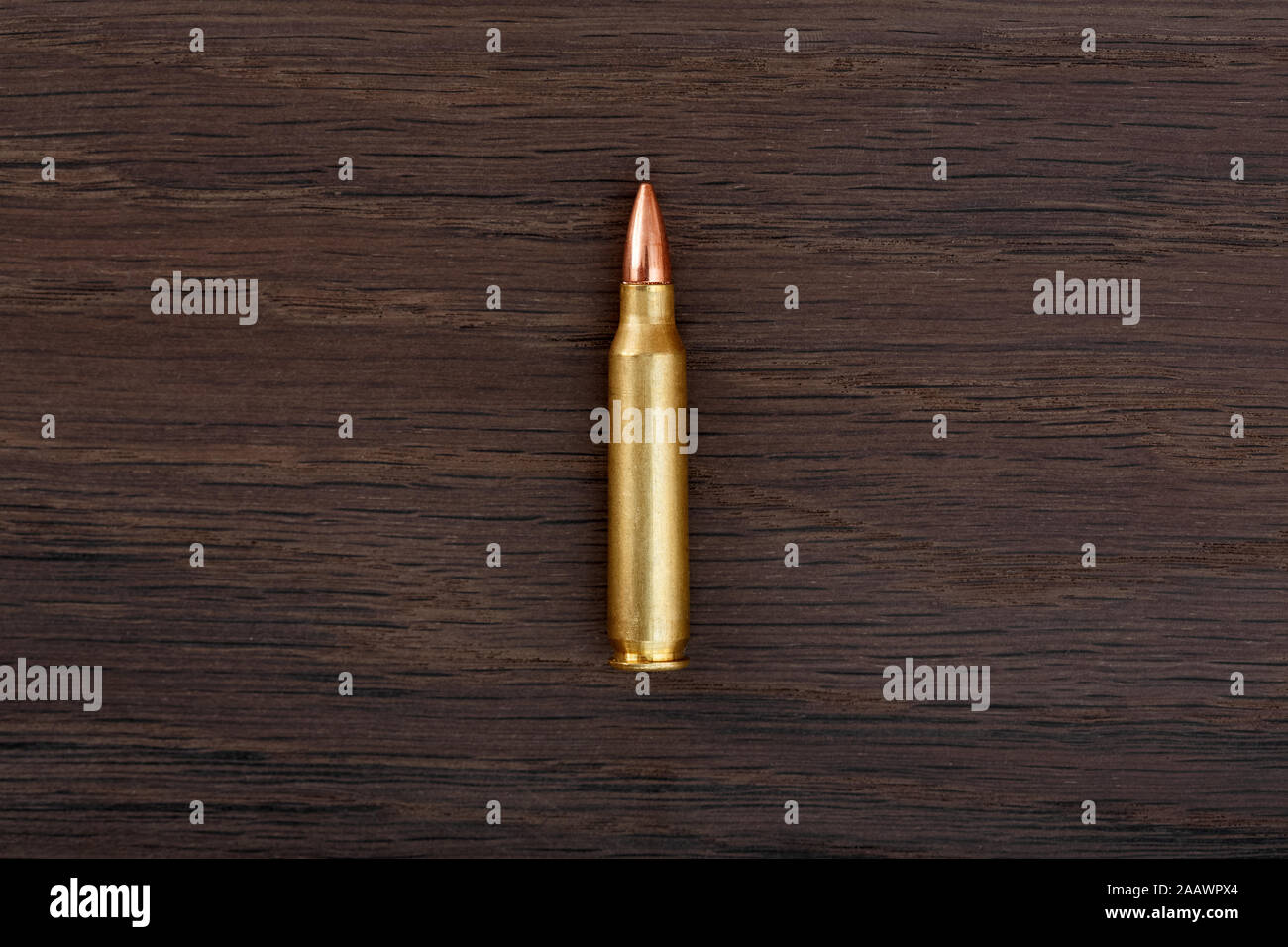 Single rifle bullet on old wooden table close-up. Stock Photo