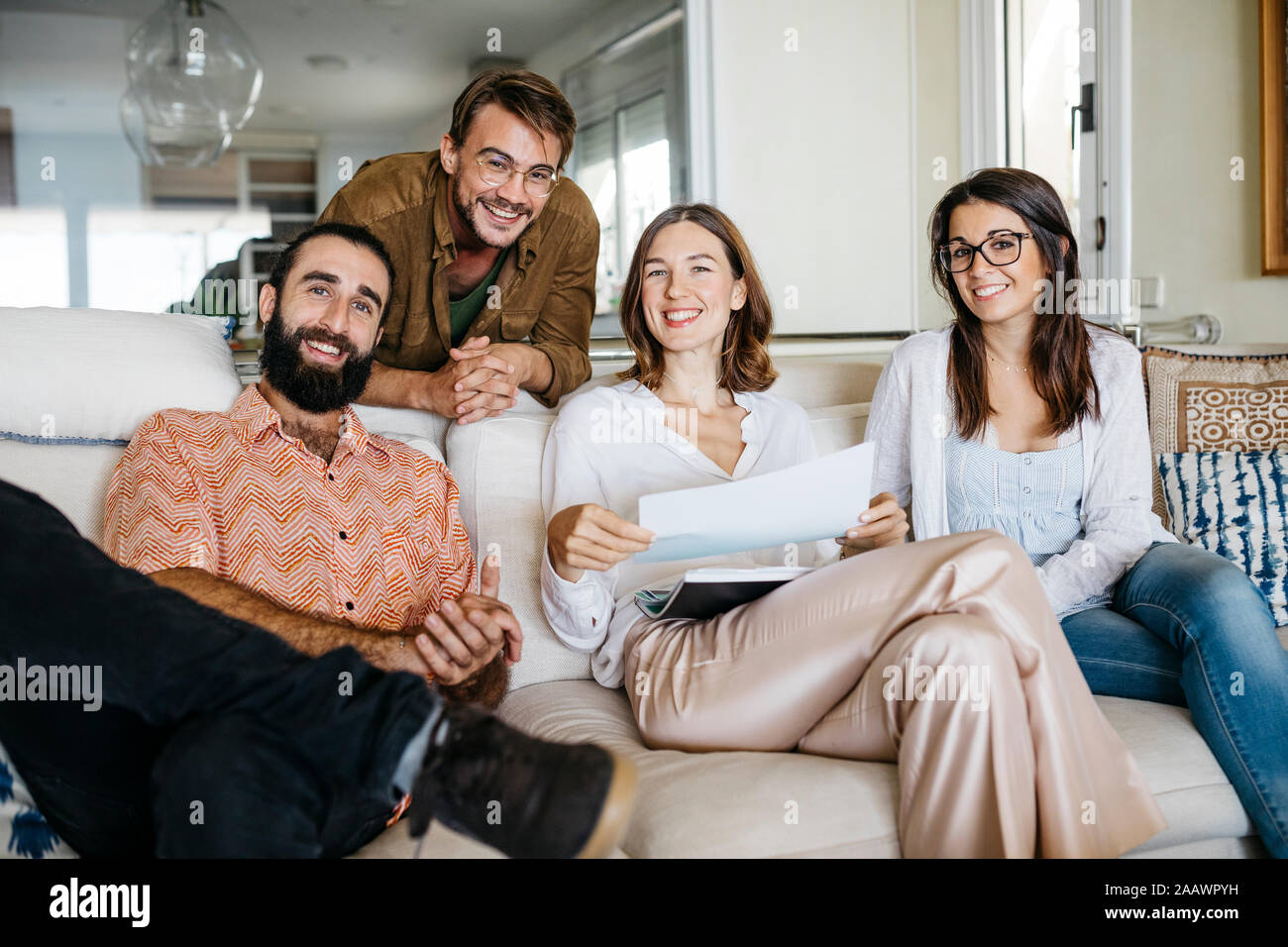 Portrait of happy friends sitting on couch with papers Stock Photo