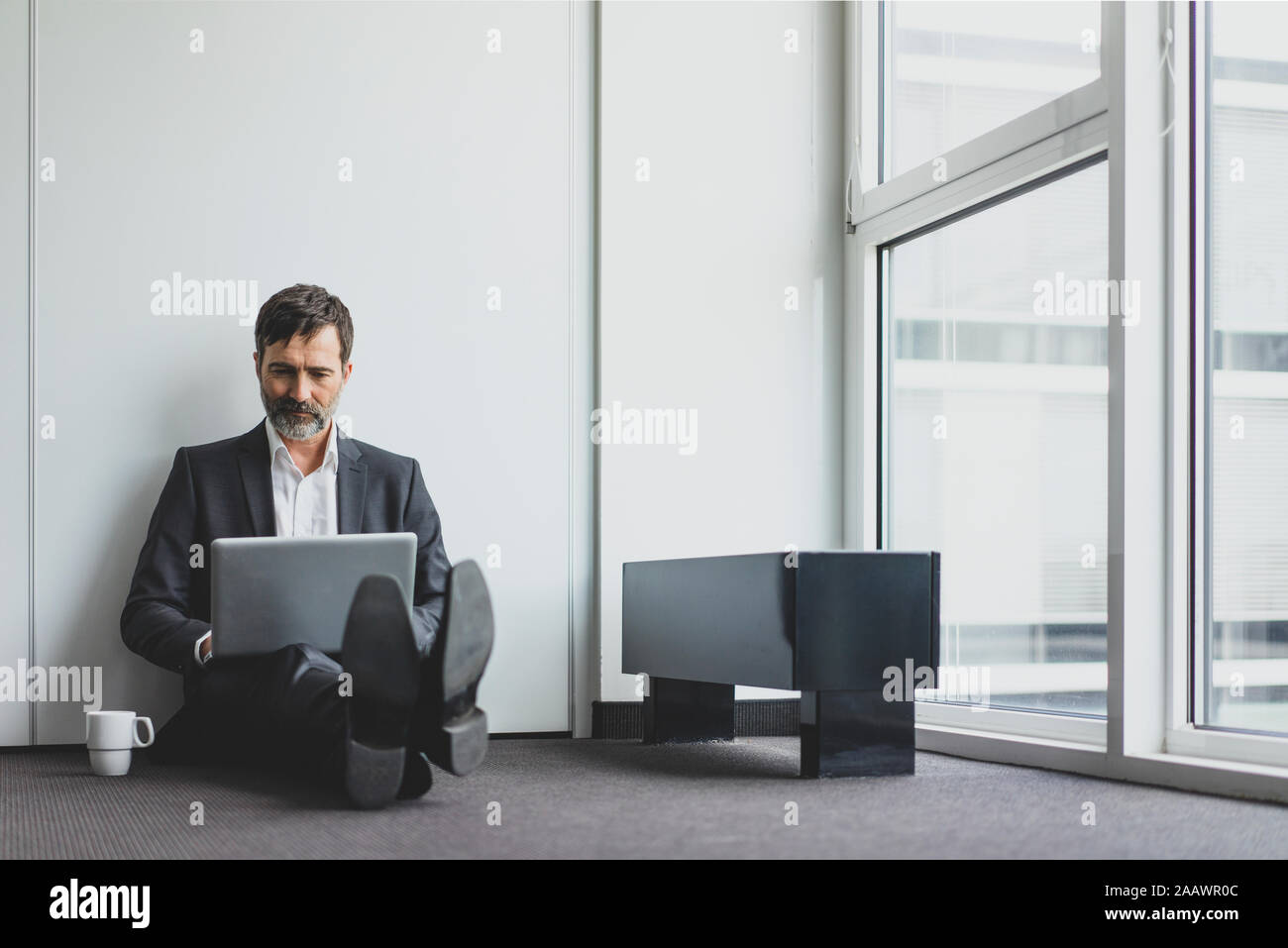 Mature businessman in office sitting on the floor using laptop Stock Photo