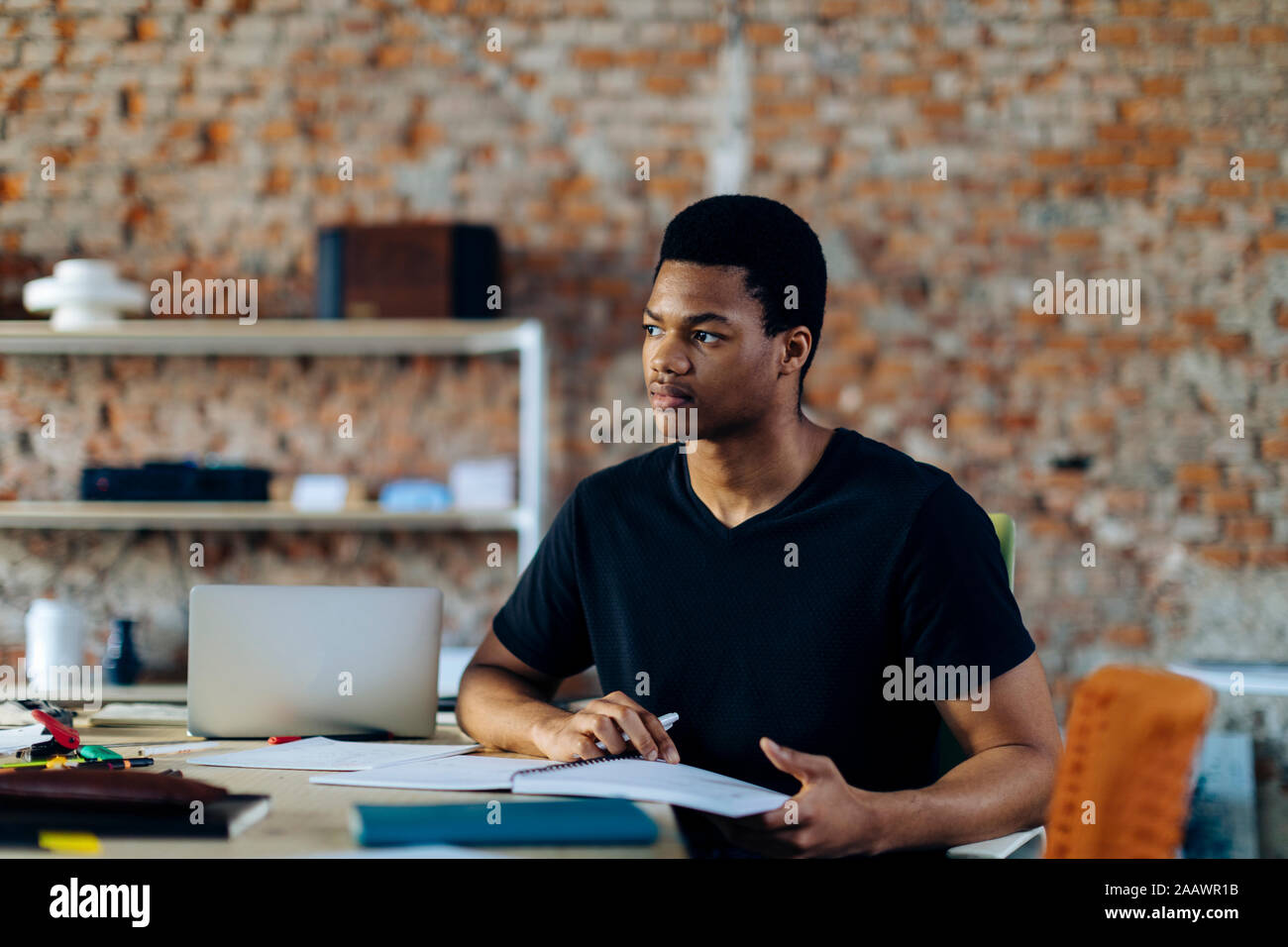 Young man sitting at table thinking Stock Photo