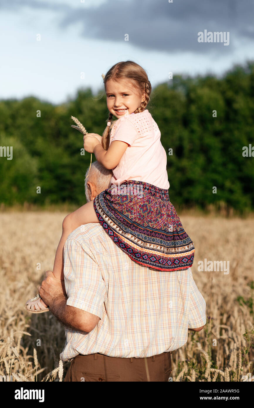 Portrait of happy little girl on grandfather's shoulders in an oat field Stock Photo