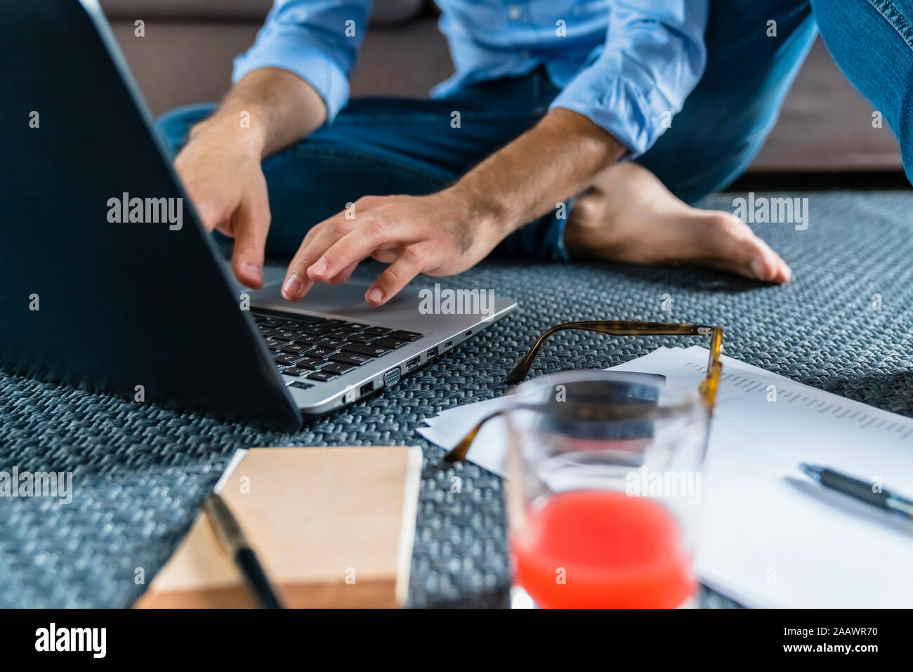 Young man sitting on the floor at home using laptop, partial view Stock Photo