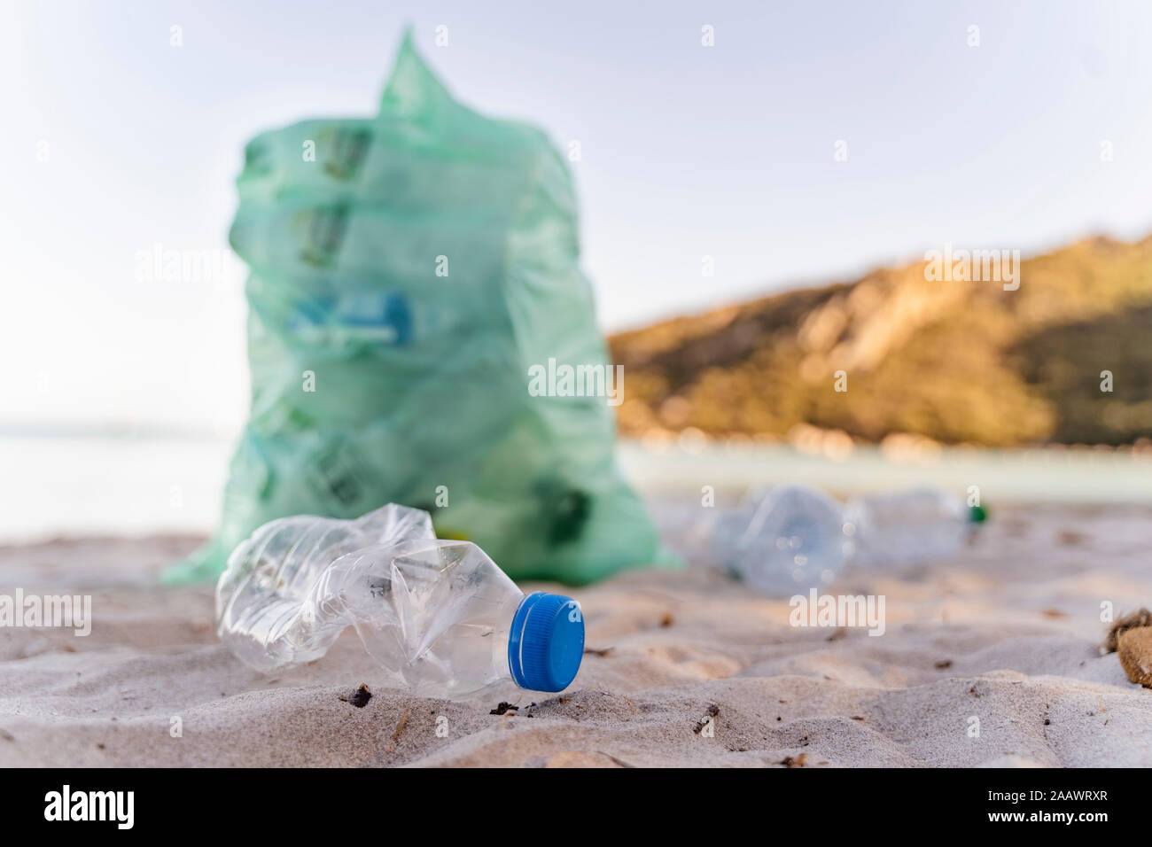 Empty plastic bottles and garbage bin full of collected plastic bottles on the beach Stock Photo