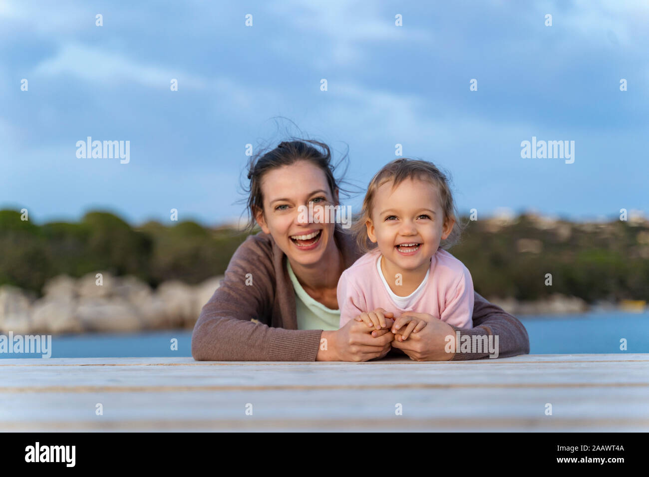 Portrait of happy mother and daughter lying on a jetty at sunset Stock Photo