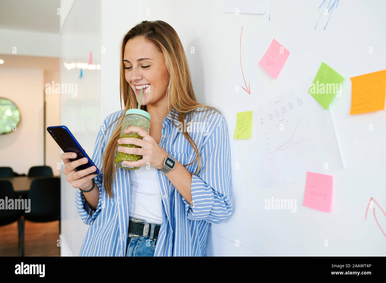Happy casual young businesswoman with drink and cell phone in an office Stock Photo