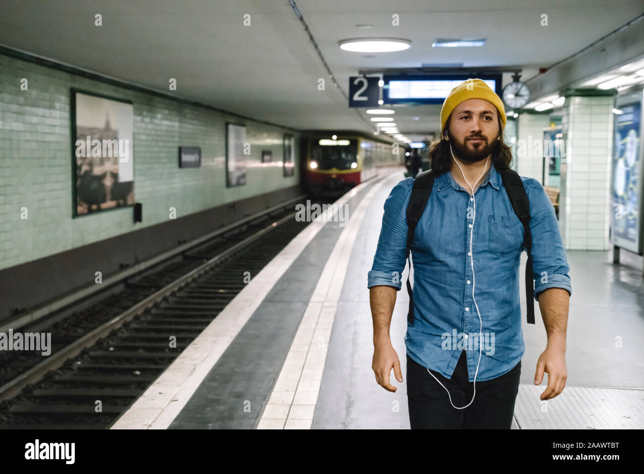 Portrait of man with backpack and earphones walking at platform, Berlin, Germany Stock Photo
