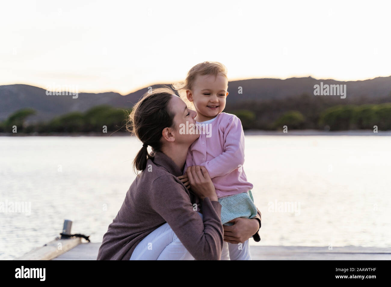 Happy mother holding her daughter on a jetty at sunset Stock Photo