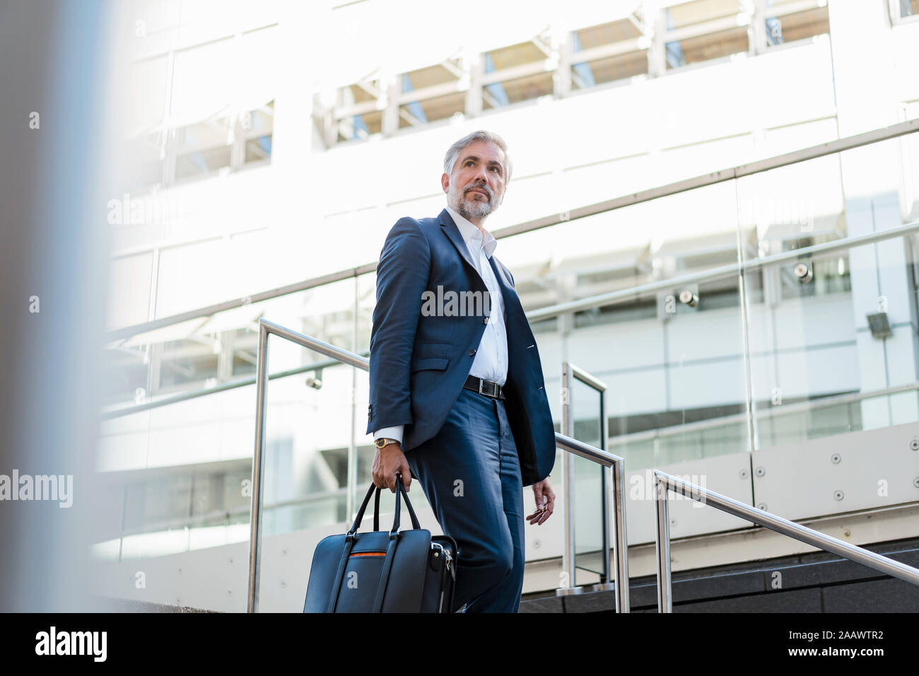Mature businessman holding bag walking down stairs in the city Stock Photo