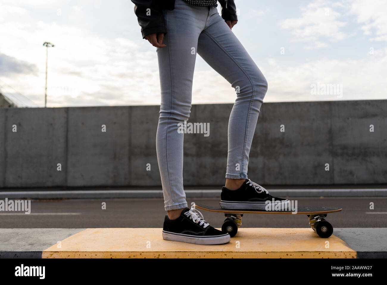 Legs of woman with skateboard standing on bollard Stock Photo