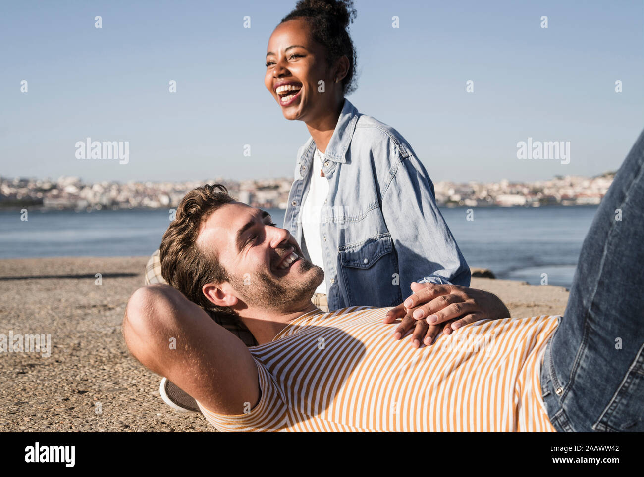 Happy young couple lying on pier at the waterfront, Lisbon, Portugal Stock Photo