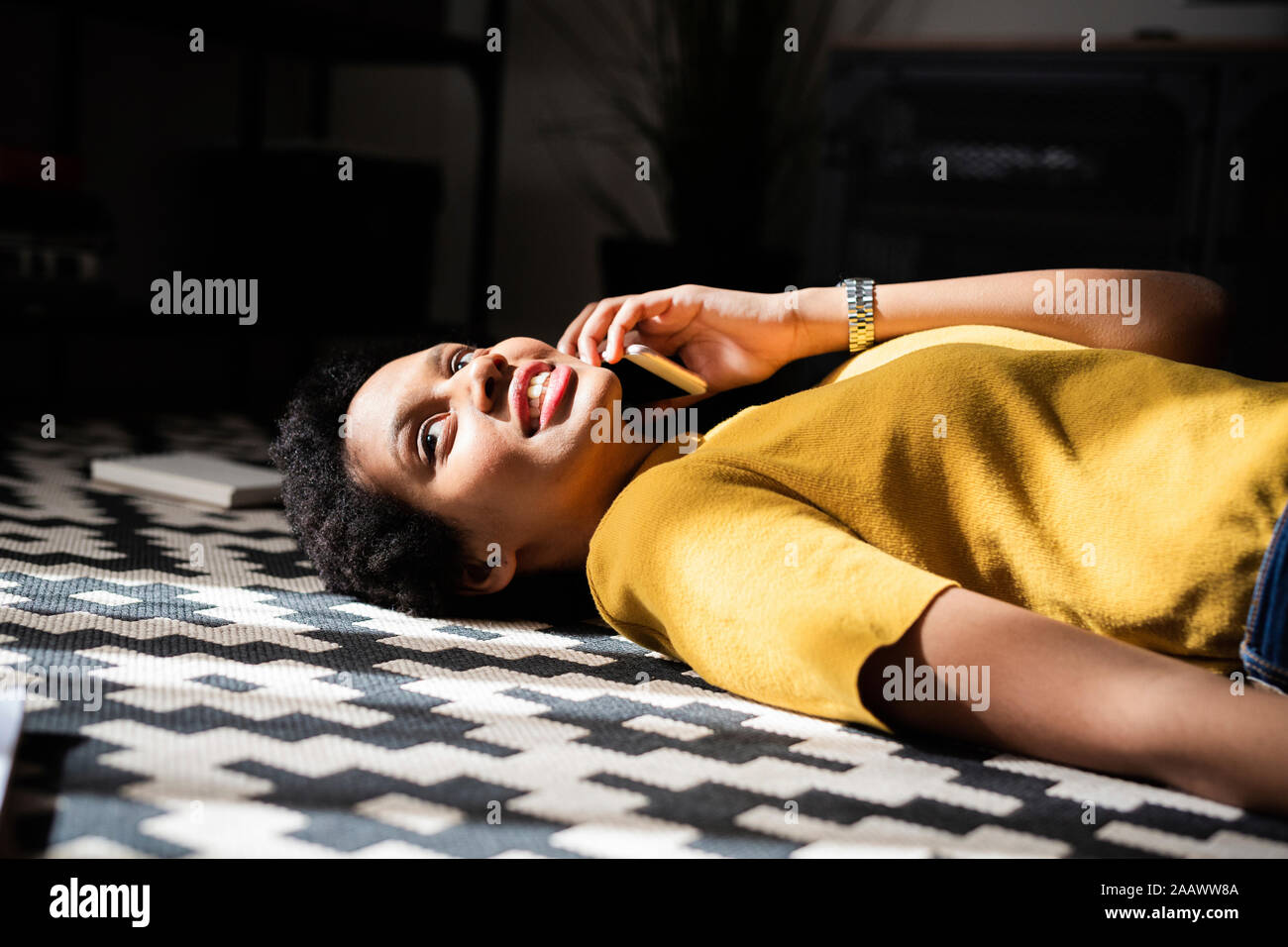 Young woman lying on the floor at home talking on the phone Stock Photo